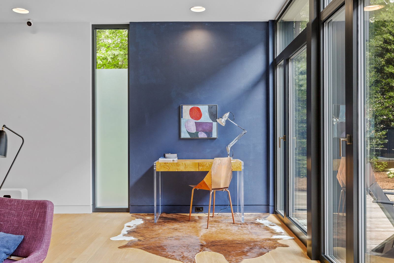Bright home office with a dramatic blue accent wall, expansive floor-to-ceiling windows, custom desk, modern lighting, and views of the surrounding landscape.